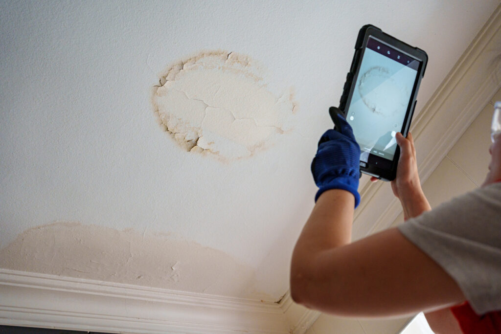 Contractor taking a photo of a stain on the ceiling caused by a roof leak. 